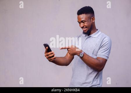 Un homme afro-américain joyeux pointant son téléphone sur fond gris Banque D'Images