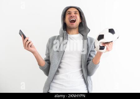 fan de football choqué dans un t-shirt bleu avec smartphone et tenant le ballon de football Banque D'Images