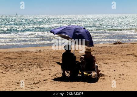 Un couple marié se protège du soleil sous un parasol sur une plage déserte Banque D'Images