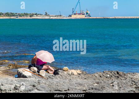 Un couple à la retraite se cache du soleil sous un parasol dans une scène industrielle Banque D'Images