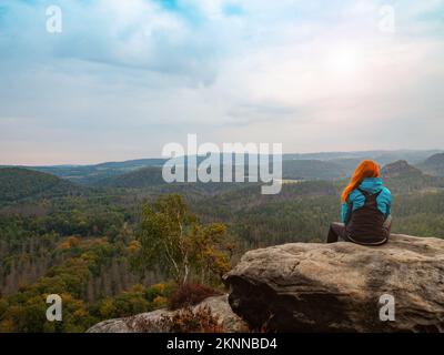 Paysage paisible. jolie fille assise sur les rochers, à loin et profiter de la nature. Vêtements de sport confortables sur son slim bod Banque D'Images