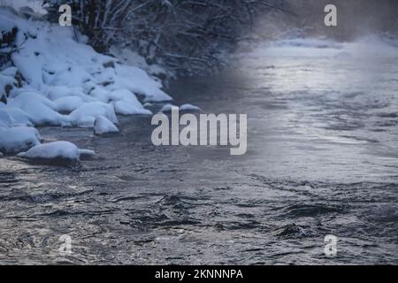 Rivière froide d'hiver, vapeur visible au-dessus de l'eau, arbres sombres des deux côtés Banque D'Images