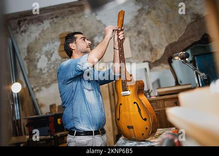 Luthier artisan fixation d'une guitare vissant la barre de treillis dans son studio-garage vintage - musique, art, artisanat et gens style de vie concept Banque D'Images