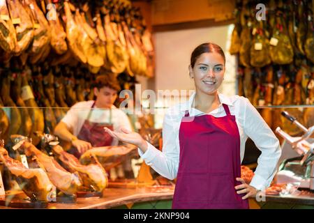 Jeune femme souriante propriétaire de boucherie en tablier offrant le jamon ibérique Banque D'Images