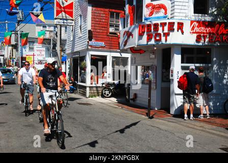 Un homme adulte passe son vélo sur la rue commerciale lors d’une journée d’été à Provicncetown, à Cape Cod. Massachusetts Banque D'Images