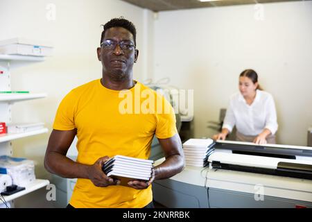 Portrait d'un sympathique employé de la maison d'impression avec pile de carnets dans ses mains Banque D'Images