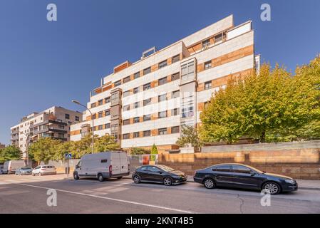 Une rue avec des voitures garées et des bâtiments résidentiels avec des arbres verdoyants un après-midi chaud Banque D'Images