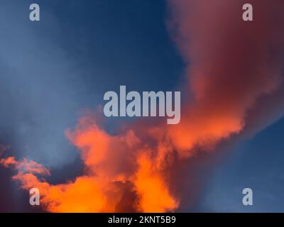 Le lever du soleil en hauteur ressemble à un feu orange vif dans le ciel bleu foncé. Les nuages sont grands et tourbillonnants. Banque D'Images