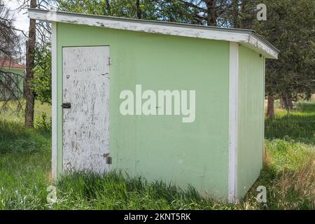 Ancien hangar de stockage peint en bois vert sur la propriété de la ferme avec de l'herbe verte haute croissance. La peinture s'écaille, la garniture et la porte sont peintes en blanc. Inclinés de toit. Banque D'Images