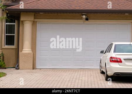 Véhicule stationné devant un grand garage double porte sur une allée pavée d'une maison américaine contemporaine typique Banque D'Images