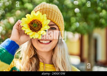 Jeune femme blonde souriant avec du tournesol à l'œil au parc Banque D'Images