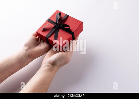 Mains tenant la boîte cadeau rouge attaché avec ruban noir, sur fond blanc avec espace de copie Banque D'Images