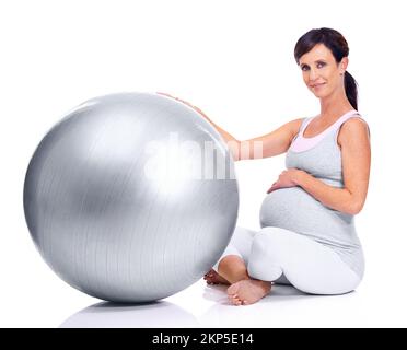 Garder la forme, jusqu'à son dernier trimestre. Une mère enceinte souriant avec une balle pilates alors qu'elle est isolée sur le blanc. Banque D'Images