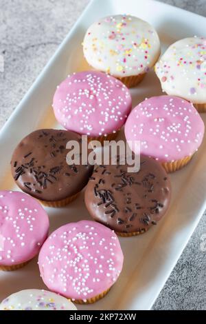 Cupcakes, décorés de glaçage et de saupoudrage sur une assiette de service blanche. Sur un fond concret Banque D'Images