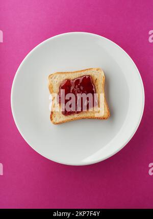 Tranche de pain grillé croustillante avec confiture de fraise sur plaque blanche et fond rose vif Banque D'Images