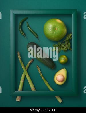 Courgettes, asperges, piment, avocat, lime, pomelo et menthe dans cadre en bois sur fond vert Banque D'Images