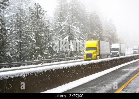 Convoi de semi-remorques industrielles de grandes rigs avec phares allumés et semi-remorques transportant des marchandises commerciales se déplaçant sur la route de la Banque D'Images