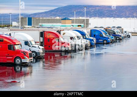 Différents font de gros engins semi-remorques les tracteurs avec semi-remorques chargées debout dans la rangée sur le parking de camion arrêter tôt le matin en attendant le Banque D'Images