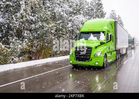 Grand semi-camion vert vif transportant des marchandises dans un réfrigérateur semi-remorque roulant devant un convoi se déplaçant lentement sur l'autoroute d'hiver pendant une sn Banque D'Images