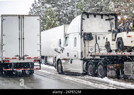 Convoi de gros engins de manutention semi-remorques avec semi-remorques transportant des marchandises commerciales sur une route glissante pendant un hiver sno Banque D'Images