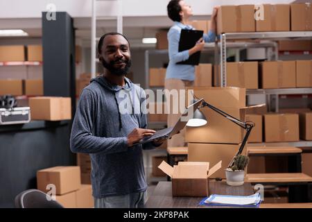 Portrait d'un responsable de magasin tenant un ordinateur portable qui regarde le stock de cargaison travaillant dans le service de livraison d'entrepôt. Divers employés préparent des colis pour les commandes des clients Banque D'Images