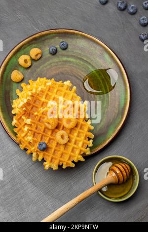 Framboises jaunes, gaufres croustillantes et une goutte de miel sur l'assiette. Balancier au miel dans un bol vert. Pose à plat. Arrière-plan gris. Banque D'Images