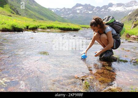 Randonneur remplissant la cantine avec de l'eau brute dans une rivière dans une haute montagne Banque D'Images