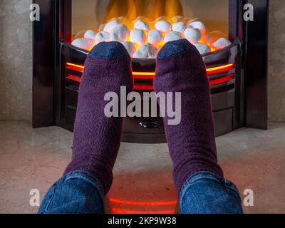 Homme réchauffant ses pieds devant un incendie à effet de charbon électrique pour éviter d'allumer le chauffage central ; crise énergétique au Royaume-Uni 2022. Banque D'Images