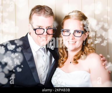Jeune mariée et marié humoristique dans des lunettes de geek stéréotypée célébrant une occasion de mariage élégante avec amour en forme de coeur Banque D'Images