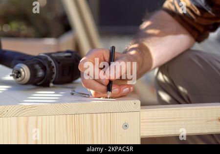 Gros plan d'une main marquant une poutre en bois sur une terrasse. Construire un lit surélevé sur un balcon au printemps. Banque D'Images