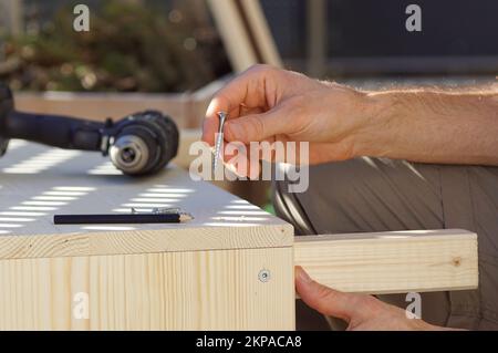 Gros plan d'une main marquant une poutre en bois sur une terrasse. Construire un lit surélevé sur un balcon au printemps. Banque D'Images