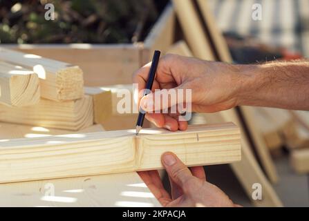 Gros plan d'une main marquant une poutre en bois sur une terrasse. Construire un lit surélevé sur un balcon au printemps. Banque D'Images