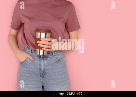 Une femme tient dans les mains une tasse de café réutilisable devant un fond rose. Concept de boissons à emporter avec place pour le texte. Banque D'Images