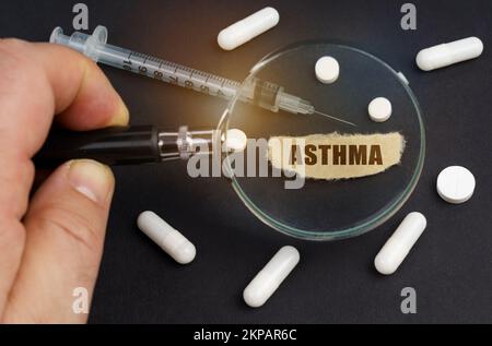 Un homme regarde à travers une loupe sur les pilules, une seringue et un morceau de papier avec l'inscription asthme Banque D'Images