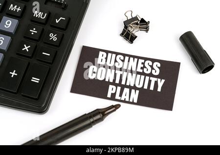 Concept commercial et financier. Sur une table blanche se trouve une calculatrice, un marqueur et une plaque noire avec l'inscription - Business Continuity Plan Banque D'Images