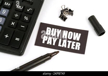 Concept commercial et financier. Sur une table blanche il y a une calculatrice, un marqueur et une plaque noire avec l'inscription - Acheter maintenant payer plus tard Banque D'Images