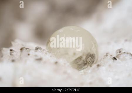 La boule de verre repose sur une neige sale ou sur un fond glacé avec des rayons du soleil. Banque D'Images