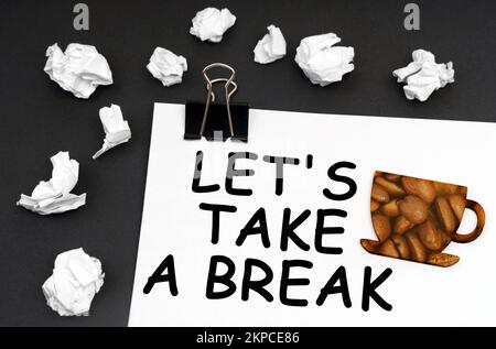 Repos au travail. Sur la surface noire se trouve une feuille blanche avec l'inscription - PRENONS Une PAUSE, une tasse avec une photo de grains de café. Banque D'Images