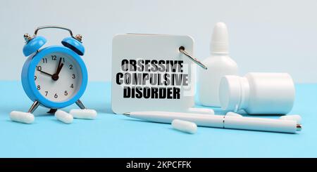 Médecine et concept de santé. Sur une surface bleue se trouvent des pilules, un réveil et un carnet avec l'inscription - trouble obsessionnel-compulsif Banque D'Images