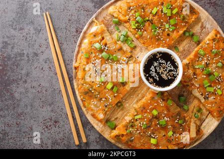 Kimchijeon est une crêpe croustillante et savoureuse coréenne faite de kimchi avec de la farine et des oignons sur le panneau en bois de la table. Vue horizontale du dessus de l'ab Banque D'Images