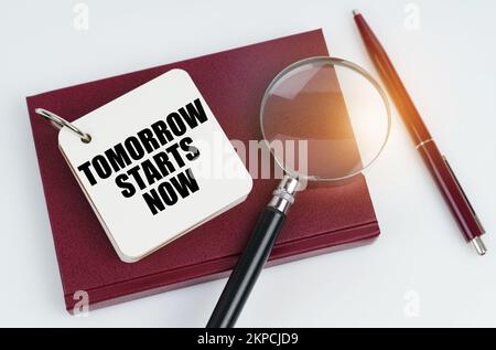 Concept commercial et financier. Sur une surface blanche se trouve un carnet rouge et un stylo, dans le carnet blanc l'inscription - DEMAIN COMMENCE MAINTENANT Banque D'Images