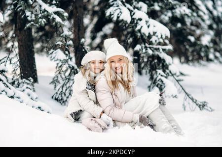 Belle mère et fille s'amusent à l'extérieur en hiver. Assis sur la neige dans la forêt entre les arbres enneigés Banque D'Images