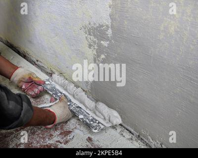 application de mastic élastique sur le mur en cours de réparation à l’aide d’une spatule large et d’un espace de copie pour le texte, mains d’un plâtre Banque D'Images