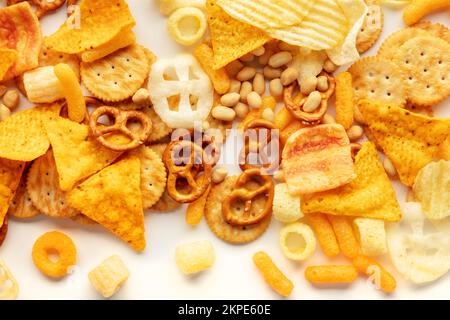 Texture des collations salées sur blanc. Assortiment de plats de fête. Chips de pommes de terre et de tortilla, craquelins et autres hors-d'œuvre, tiré par le haut Banque D'Images