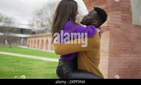 Couple Interracial heureux. Jeune femme sautant dans les bras de petit ami au parc Banque D'Images