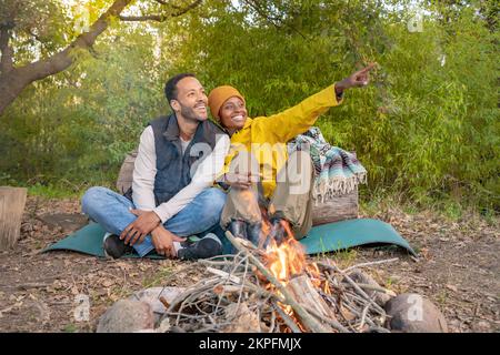 Couple multiethnique assis à l'extérieur autour du feu du camp. Profiter de la vie saine de la nature Banque D'Images