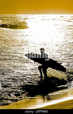 Silhouette d'un surfeur entrant dans la mer avec sa planche de surf pendant le coucher du soleil à la plage d'Ipanema à Rio de Janeiro Banque D'Images