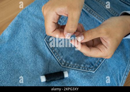 Mains d'une couturière enfilant une aiguille sur le fond d'un Jean Banque D'Images