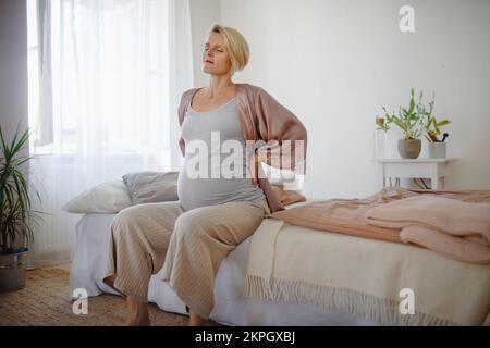 Femme enceinte assise sur son lit et se reposant. Banque D'Images