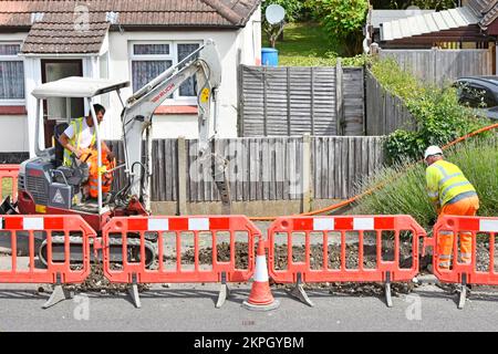 Le conducteur d'excavateur de mini-excavateur brise la chaussée pour le câble à large bande de fibre optique de couleur orange dans une nouvelle tranchée assistée par le ouvrier de banque Essex UK Banque D'Images